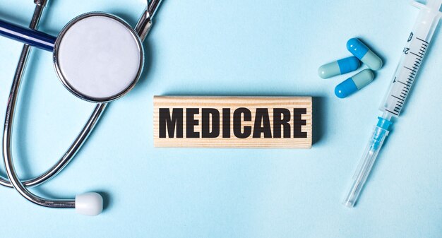 On a blue background, a stethoscope, a syringe and pills and a wooden block with the word medicare. medical concept