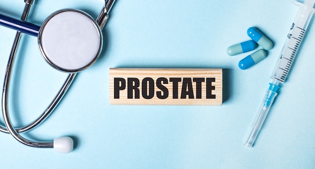 Su uno sfondo blu, uno stetoscopio, una siringa e pillole e un blocco di legno con la parola prostata. concetto medico