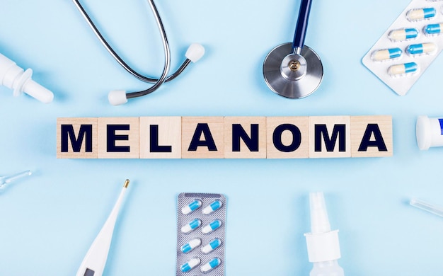 On a blue background a stethoscope a thermometer other medicines and wooden cubes with the text MELANOMA View from above Medical concept