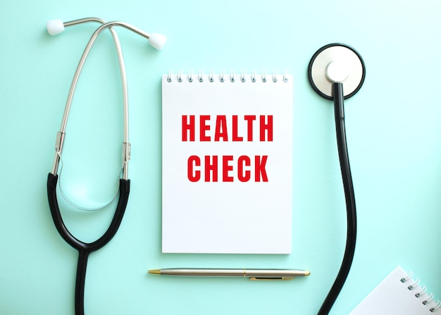 On a blue background a stethoscope and a white notepad with the red words HEALTH CHECK