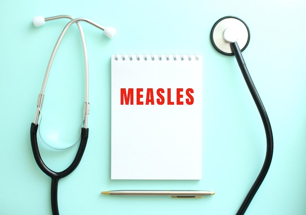 На синем фоне стетоскоп и белый блокнот с надписью MEASLES.