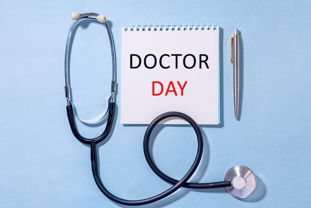 Photo on a blue background stethoscope with notepad and pen text doctor day