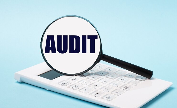 Photo on a blue background, a white calculator and a magnifying glass with the text audit. business concept