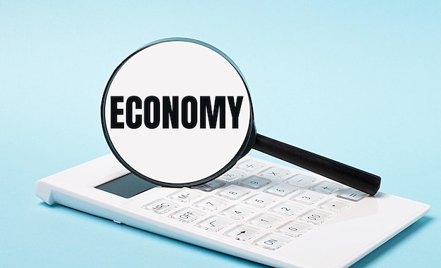 Su uno sfondo blu una calcolatrice bianca e una lente d'ingrandimento con il testo economia business concept