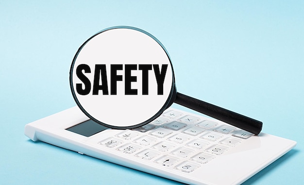 On a blue background a white calculator and a magnifying glass with the text SAFETY Business concept