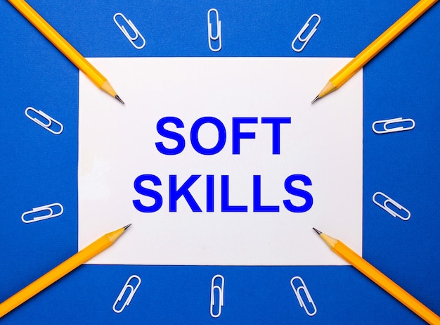 On a blue background white paper clips yellow pencils and a white sheet of paper with the text SOFT SKILLS