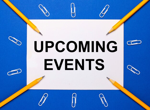 On a blue background, white paper clips, yellow pencils and a white sheet of paper with the text upcoming events