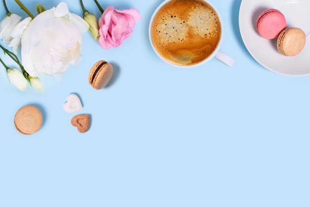 Blue background with cup of tasty coffee macaroons peonies and roses Top view with space for your text