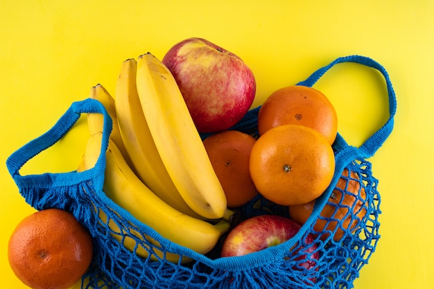 Blue bag string bag with bananas, red apples and tangerines