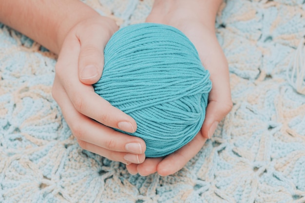 Blue ball of wool in hands against the background of a green knitted tablecloth. High quality photo