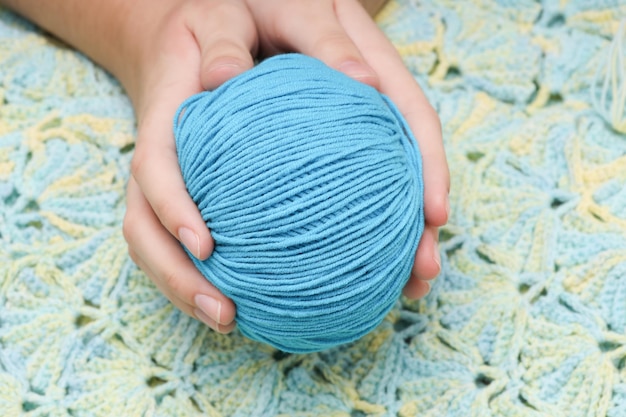 Blue ball of wool in hands against the background of a green knitted tablecloth. High quality photo