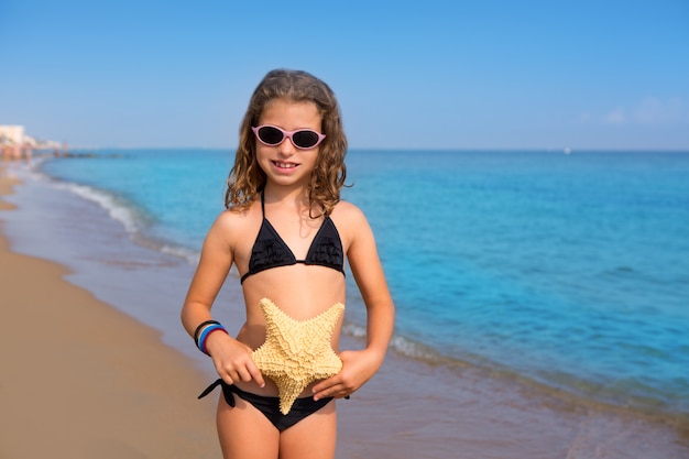 Foto ragazza spiaggia blu con stelle marine bikini e occhiali da sole