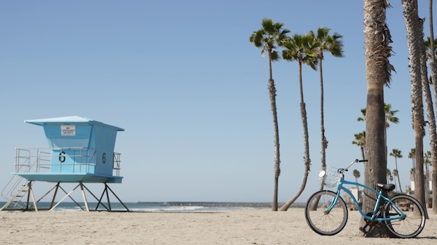 Blue bicycle, cruiser bike by ocean beach, sea coast,  palm trees, lifeguard tower watchtower hut