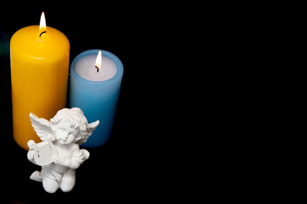 Photo blue big lit candle and ceramic white angel on black background.mourning.memory of the deceased