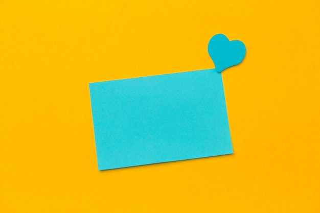 Photo blue blank paper sheet and pink hearts on a yellow background copy space