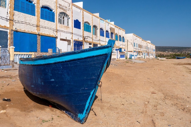 Foto una barca blu è bloccata sulla spiaggia di fronte agli edifici del villaggio di pescatori di tafelney