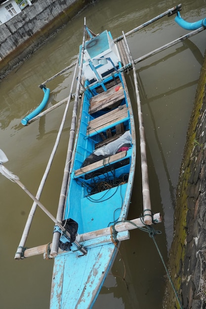 A blue boat with a white seat is docked in a river.
