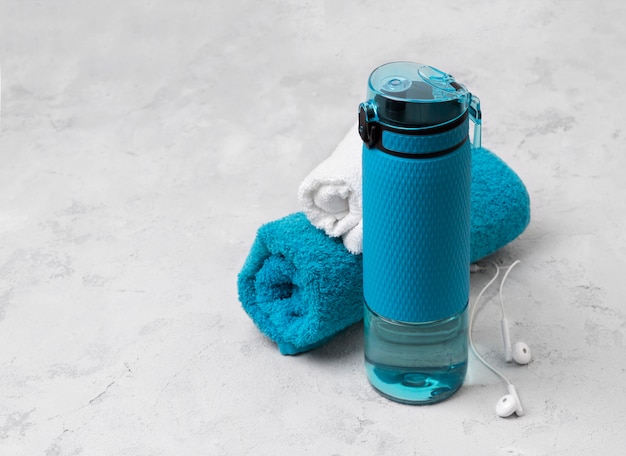 Blue bottle of water and towels. Sports equipment on gray concrete table