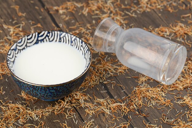 Blue bowl of fresh milk and scattered saffron on wooden surface