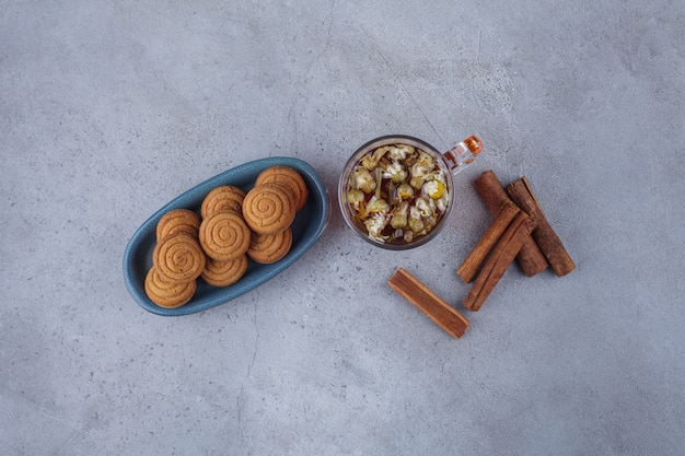 Blue bowl of mini cinnamon cakes with glass of tea on stone surface. 