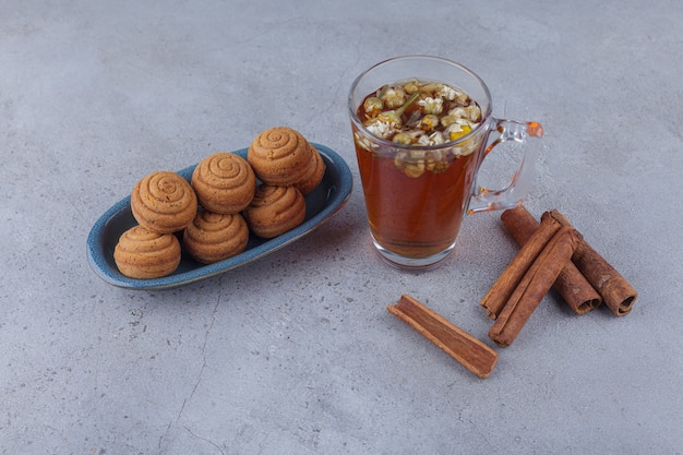 Blue bowl of mini cinnamon cakes with glass of tea on stone.