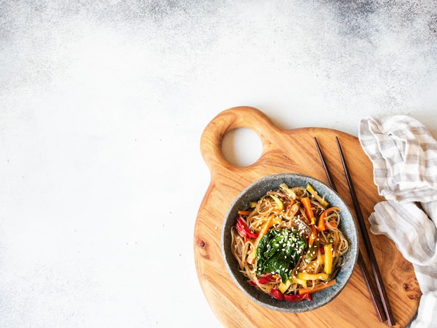 Blue bowl with rice noodles and various vegetables steer fry on a wooden board on grey