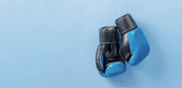 Blue boxing gloves hang on a blue wall Template Copy space for text mockup