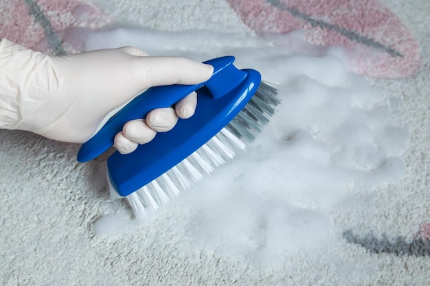 Photo blue brush on the floor with hand in rubber glove cleaning