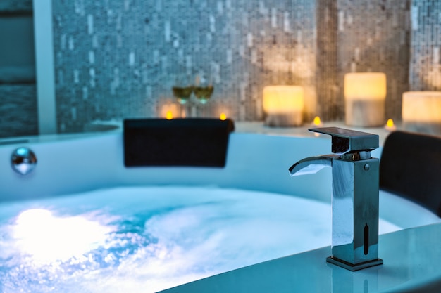 Acqua blu gorgogliante nella vasca idromassaggio close-up rubinetto decorato con candele sullo sfondo,