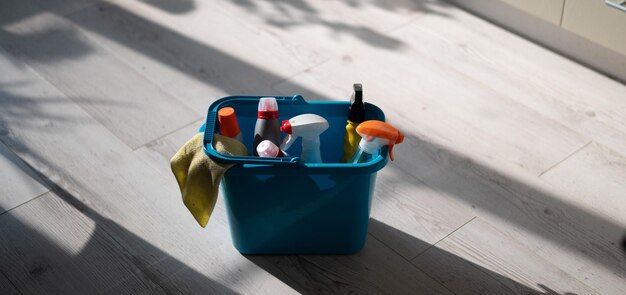 Blue bucket with cleaning products on the laminate Set of detergents and a rag for home cleaning on a wooden floor in the apartment No people