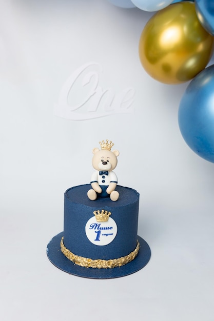 A blue cake with a teddy bear on top with a crown on it Cyrillic inscription Misha is 1 year old