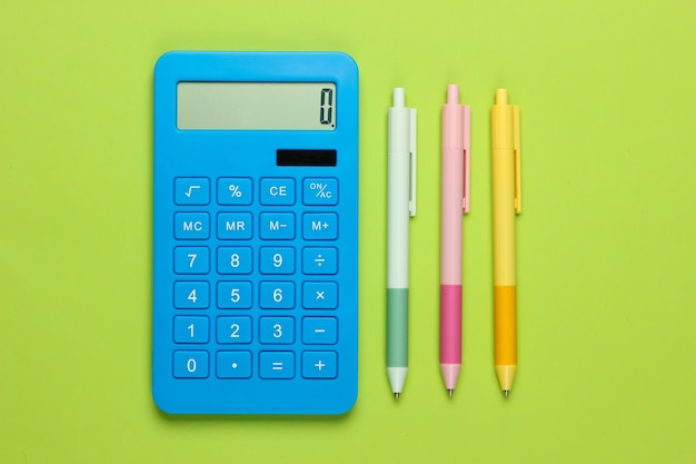 Blue calculator with colored pens on a green. Office tools. Economist