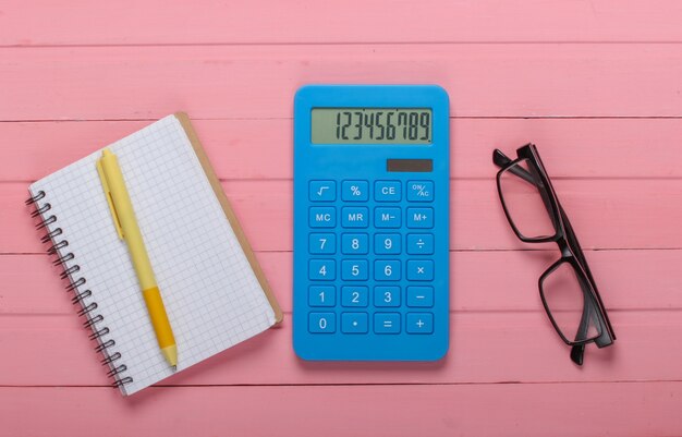 Blue calculator with notebook and glasses on pink wooden