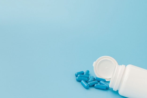 Blue capsules, pills on a blue background. Capsules in a white jar. Vitamins, nutritional supplements for women's health