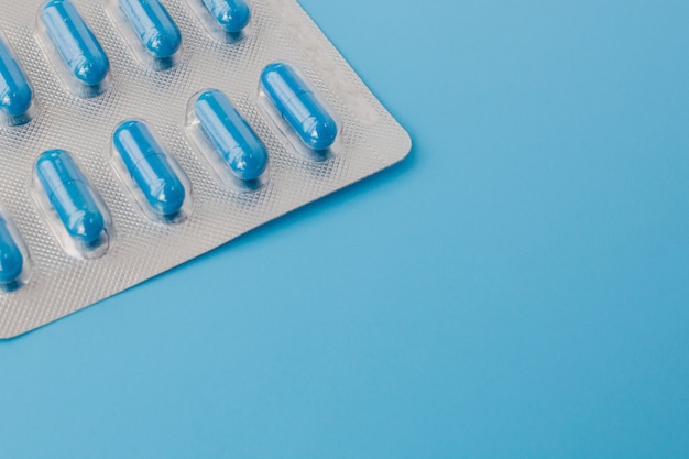 Blue capsules, pills on a blue wall. Vitamins, nutritional supplements for women's health