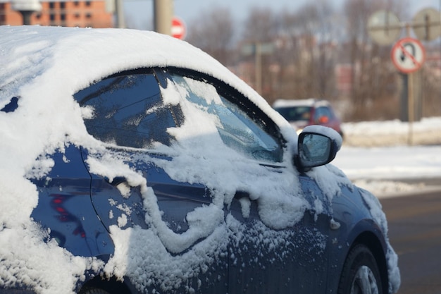 Blue car covered with snow riding on winter day street