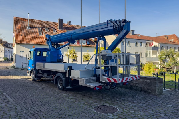 A blue car with a hydraulic lift for people stands on a paved sidewalk in front of residential