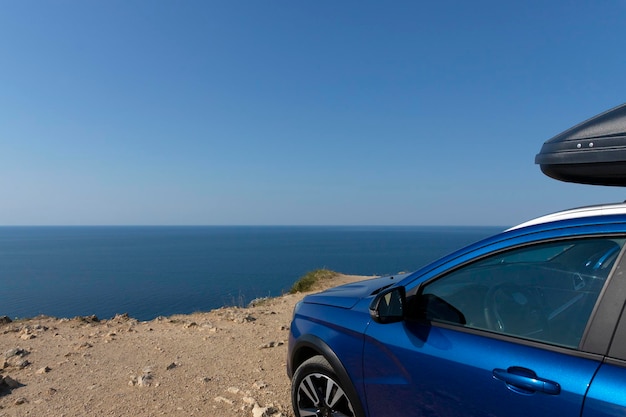 A blue car with a roof rack on the edge of a cliff against the blue sky and the sea Car travel concept High quality photo