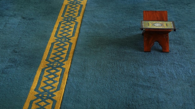 A blue carpet with a blue rug with a yellow border and a small wooden stool on top.