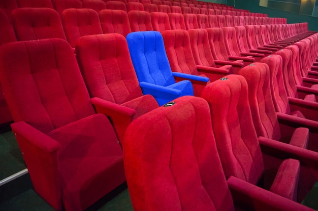 Blue chair between rows of red seats in the modern theater. Concept cinema scene