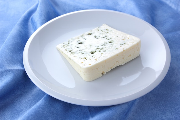 Blue cheese. Cheese on a white plate. Dairy product on a blue napkin