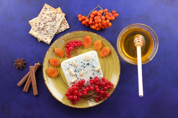 Фото Сыр с плесенью с орехами, ягодами и сухофруктами на желтой тарелке сыр с медовыми булочками и специями на синем фоне крупным планом