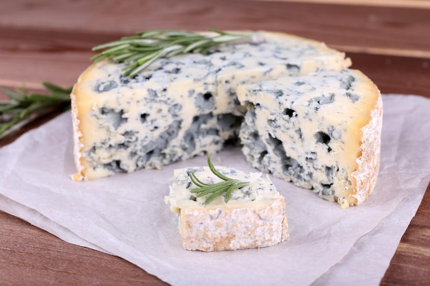 Blue cheese with sprigs of rosemary on sheets of paper and wooden table background