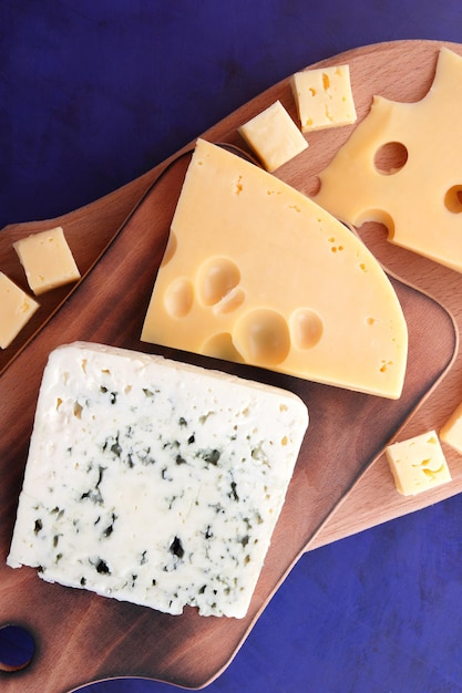 파란색 배경에 있는 나무 판자에 있는 파란색 치즈와 노란색 하드 치즈 다양한 종류의 치즈 구성 근접 촬영