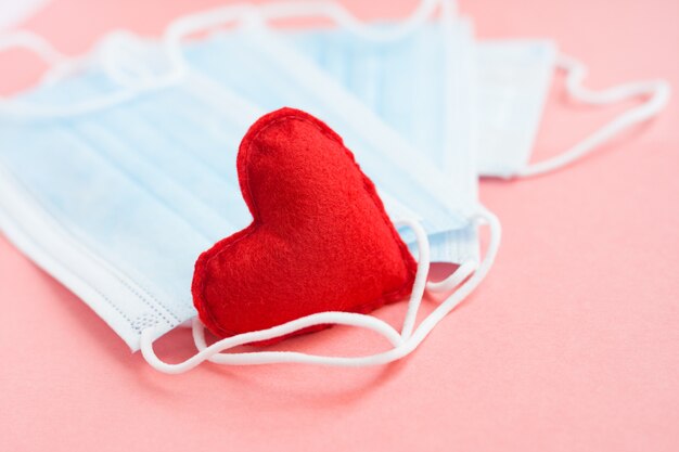 Blue cloth medical masks with red heart on pink background. Brave heart and gratitude to all workers of medicine. Coronavirus, COVID-19, pandemic during quarantine.