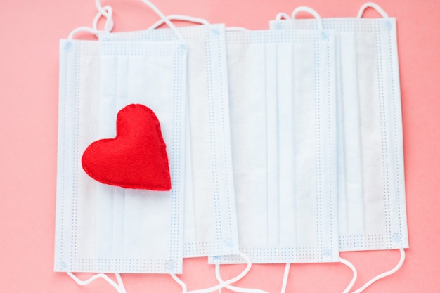 Blue cloth medical masks with red heart on pink background. Brave heart and gratitude to all workers of medicine. Coronavirus, COVID-19, pandemic during quarantine.