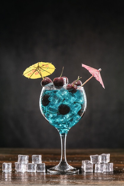 Blue cocktail in a glass with ice and cherries