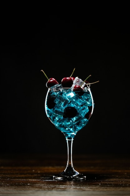 Синий коктейль в бокале со льдом и вишней