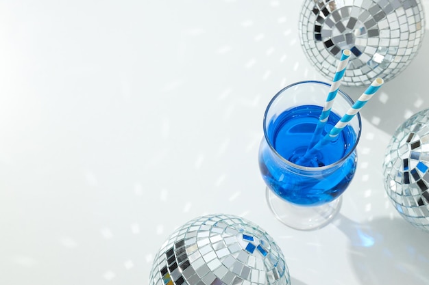 Blue cocktail with straws in glass and disco balls on white background space for text