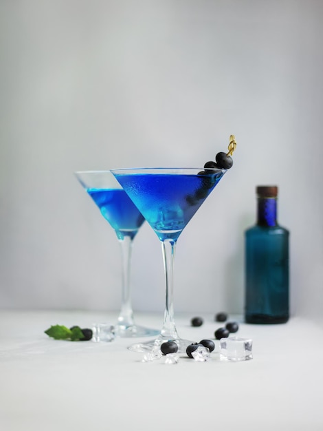 Photo blue cocktails in martini glass with ice cubes mint and bluberries and bottle of gin